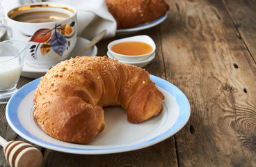 Fresh croissant, a cup of coffee and honey on a wooden table       