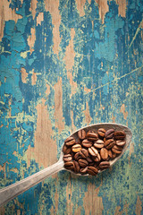 Coffee beans in a spoon on wooden background