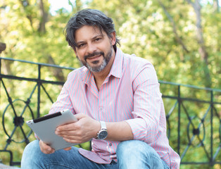 Happy adult handsome man sitting outdoors and tablet