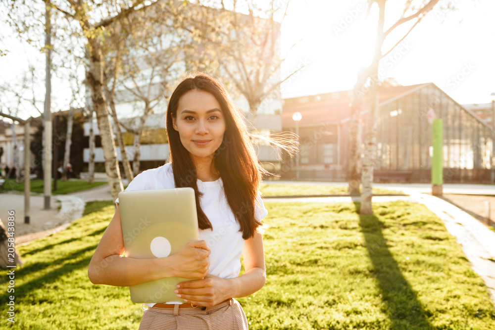 Poster Happy woman walking in park outdoors holding laptop