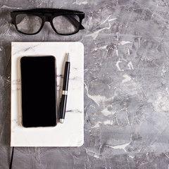 Notepad, mobile phone, pen, succulent, glasses, cup of coffee on a gray cement background.