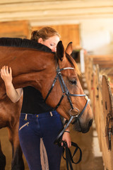 Jockey young girl petting and hugging brown horse