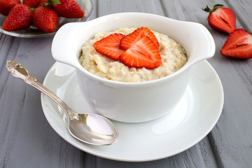 Oatmeal with  strawberry  in the white plate on the grey wooden background