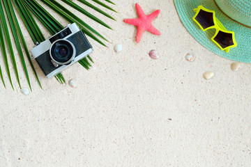 Beach background.  Top view of beach sand with coconut leaves, camera,  shells, starfish, sunglasses, shells and straw hat. Summer background concept.
