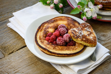Sweet homemade pancakes with raspberry on a plate decorated with flowers of an apple tree on a wooden background.