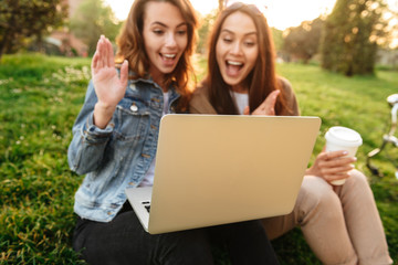 Two young beautiful happy women friends outdoors using laptop computer