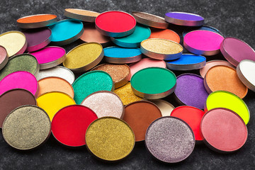 big amount of shimmer and matt multicolored circle shaped eye shadows lying on a black background. concept of healthy make up products