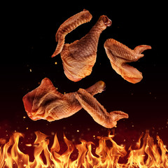 Flying raw chicken pieces above grill flames