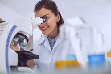 Good mood. Alert professional biologist wearing a uniform and looking into the microscope