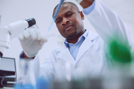 Conducting a test. Unsmiling skilled researcher wearing a uniform and doing a test