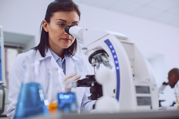 Challenging research. Determined experienced scientist working with her microscope and wearing a...
