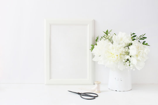 White blank wooden frame mockup. Wedding table still life composition with floral bouquet made of peony and Gypsophila flowers, silk ribbon and vintage scissors on the table. Home decor.