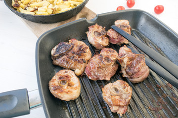 Grilled turkey pieces grilled in a frying pan, tomatoes and fried potatoes in the background, located on a light background