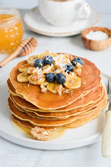 Stack of tasty pancakes with banana, blueberry, walnuts and honey