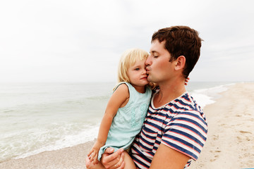 Father holds daughter on his hands and kisses her on the forehead. Family vacation by the sea.