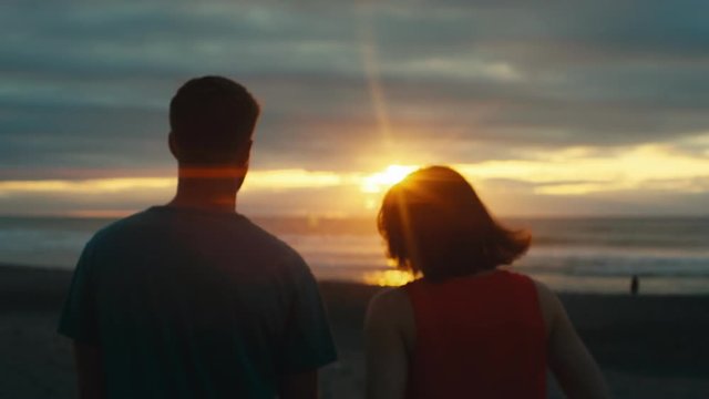 Slow motion couple walking on beach at sunset with anamorphic flares