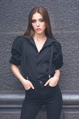 Beautiful girl in black clothes oversize with suspenders. Dark background. Toned image.