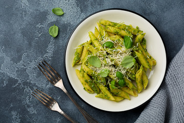 Penne rigate pasta with parmesan cheese and basil leaves in ceramic plate on gray vintage old concrete background. Selective focus.