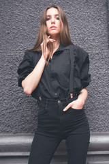 Beautiful girl in black clothes oversize with suspenders. Dark background. Toned image.