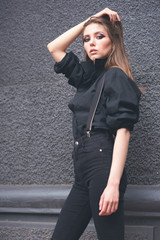 Beautiful girl in black clothes oversize with suspenders. Dark background. Toned image.