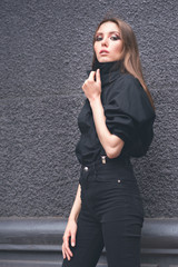 Beautiful girl in black clothes oversize with suspenders. Dark background. Toned image.