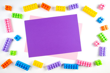 Colorful plastic construction blocks frame with violet blank card on white background