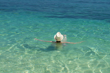 Young girl with white hat swimming and enjoying life in tropical ocean