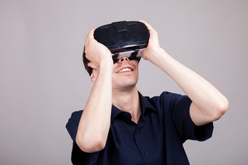 Excited man experiencing virtual reality for the firts time. He is wearing a VR headset. Gray background. Studio photo