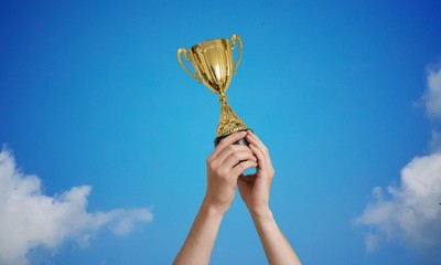 Winner is holding a trophy in hands against blue sky.