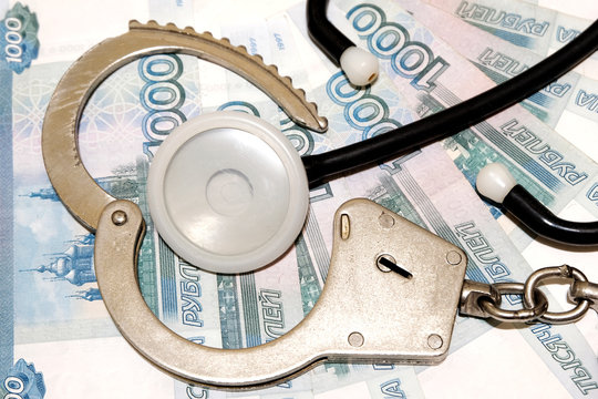 An open bracelet of police handcuffs and a medical phonendoscope lie on the background of Russian money. Violation of the law in the field of medicine. Corruption of doctors in Russia.