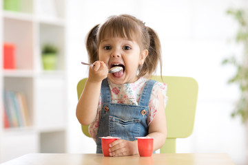 Cute little child girl eating yogurt indoors