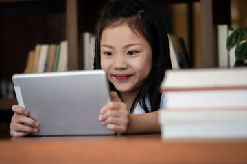 cute girl smile sitdown and playing tablet smartphone in the library, children concept, education concept