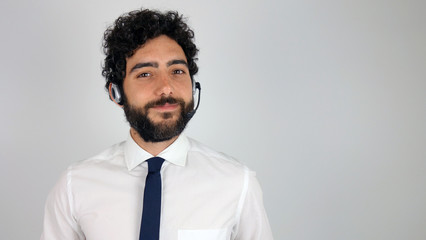 Handsome consultant of call center in headphones on gray background. Young and brunette man smiling looking at the camera.