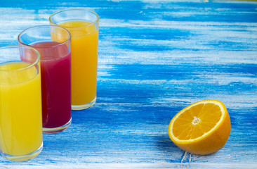 Three glasses of soft drinks are on a blue background. Slices of an orange. Summer drinks and healthy lifestyle.
