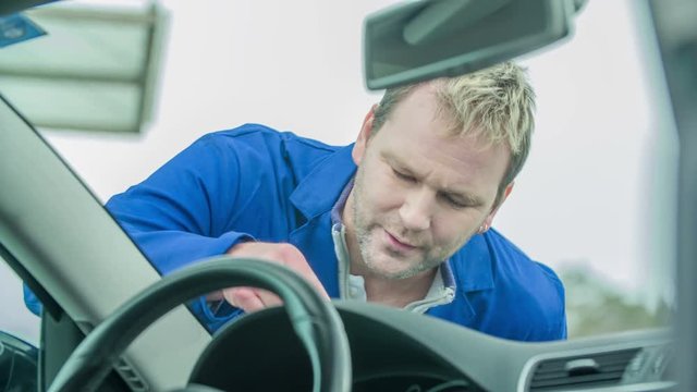 A man checks the crack on the front window of the car and then he looks annoyed.