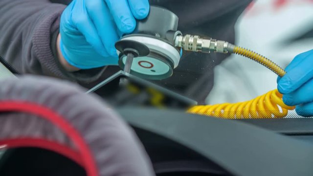 A mechanic is checking the front window on the car and he is using a special device.