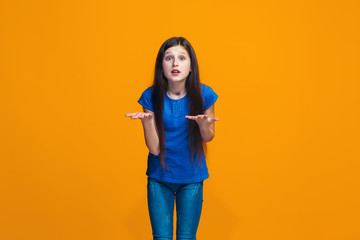 Beautiful female half-length portrait on orange studio backgroud. The young emotional teen girl
