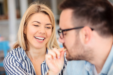Happy young woman feeding her boyfriend. Playful couple sitting in a cafe and having breakfast