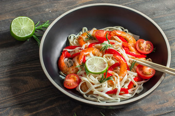 Fried shrimp with Udon noodles, paprika and rosemary in a black plate