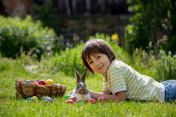 Cute child, playing with little bunny and easter eggs in a blooming garden, springtime © Tomsickova