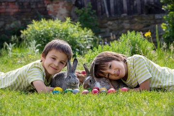 Cute child, playing with little bunny and easter eggs in a blooming garden, springtime