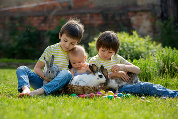 Cute children, boy brothers, toddler and preschool, playing with little bunnies and easter eggs in a blooming garden