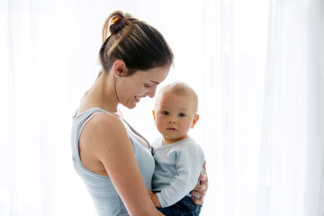 Young mother, embracing with tenderness and care her baby boy, smiling happilye