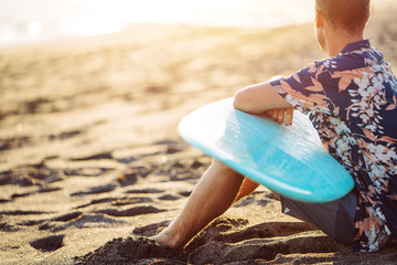 Man surfer with surfboard sitting and resting on the beach near the ocean