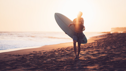 Happy surfer running on the beach near the ocean with short surfboard