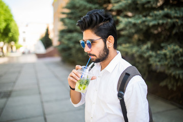 Closeup portrait, young happy handsome man drink cold drink mojito on city street background on a sunny day