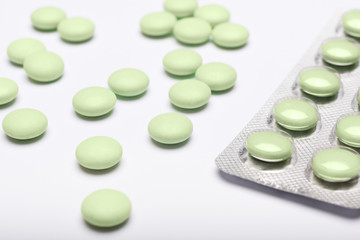 Green pills and blister pack on white background. Pharmaceutical industry minimal still life background. Opioid epidemic and drug abuse concept.