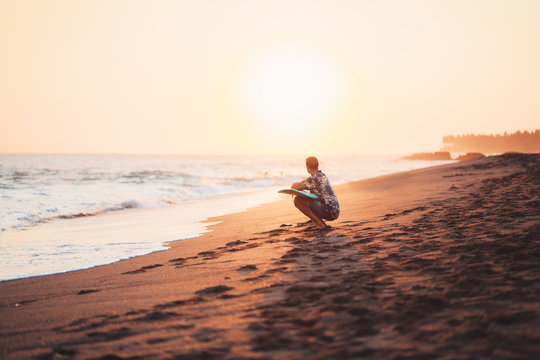 Man surfer resting on the beach near the ocean with short surfboard at sunset