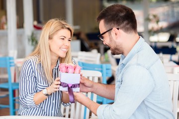 Happy young woman is receiving flower bouquet from her boyfriend as a birthday or anniversary gift. Romantic moments in a cafe