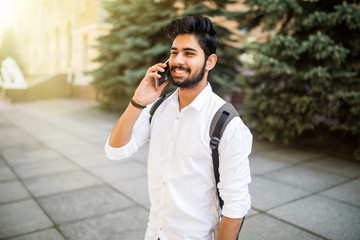 Portrait of a young handsome Indian man talking on phone on the street